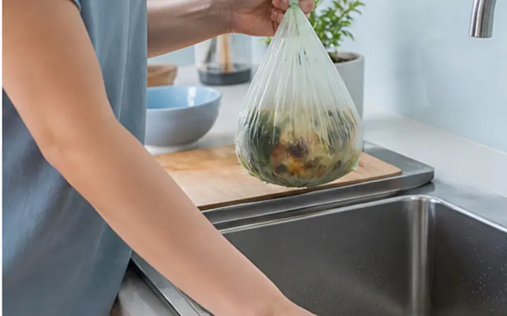 Seseorang membersihkan wastafel sambil membawa kantong sampah organik basah